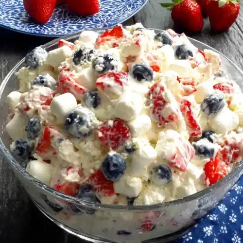 Red, white & blue cheesecake salad with strawberries, blueberries, and marshmallows in a glass dish