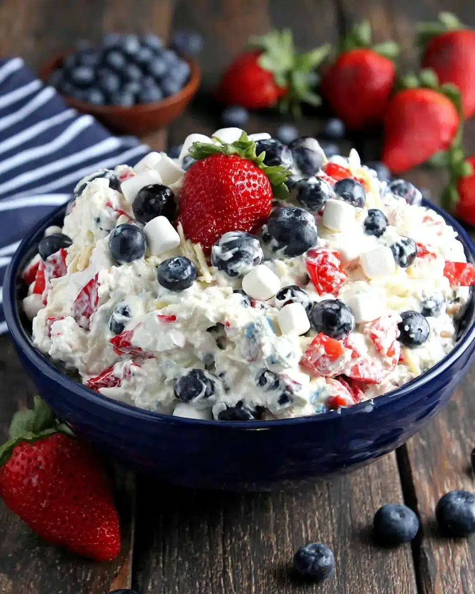Red white & blue fluff salad with strawberries, blueberries, and marshmallows in a blue bowl