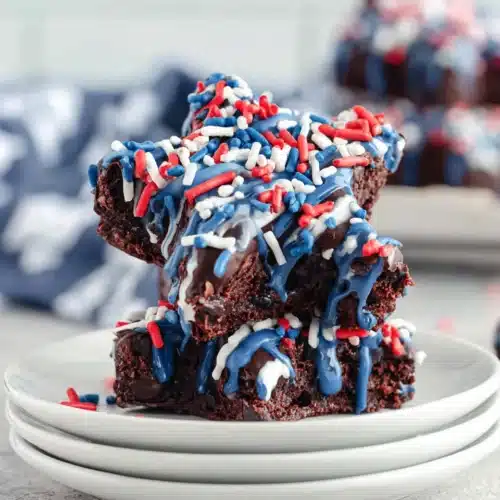 Star spangled brownies with blue drizzle and red, white, blue sprinkles on white plates