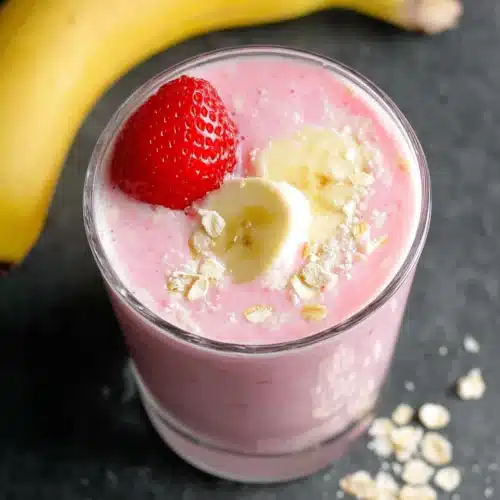 Strawberry banana smoothie with yogurt in a glass, topped with banana slice and strawberry
