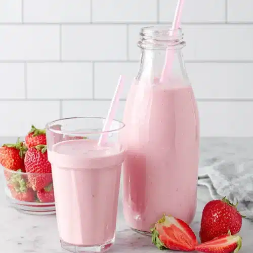 Strawberry smoothie with yogurt in glasses and bottle, fresh strawberries nearby