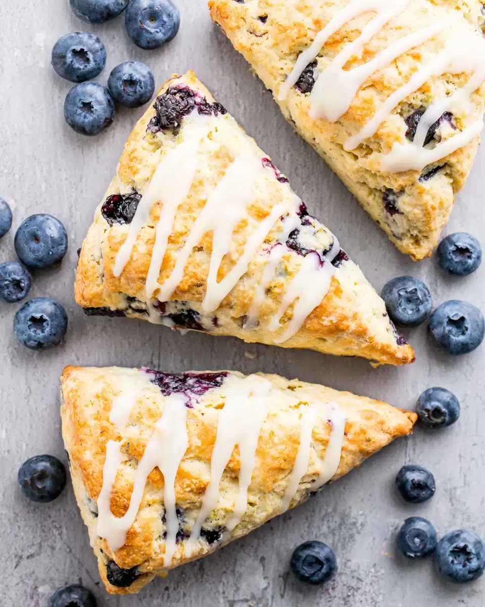 Vegan blueberry scones with white glaze and fresh blueberries on a gray surface