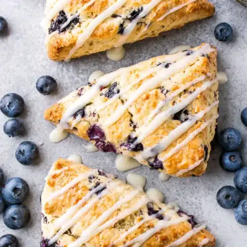 Vegan blueberry scones with white glaze and fresh blueberries on a gray surface