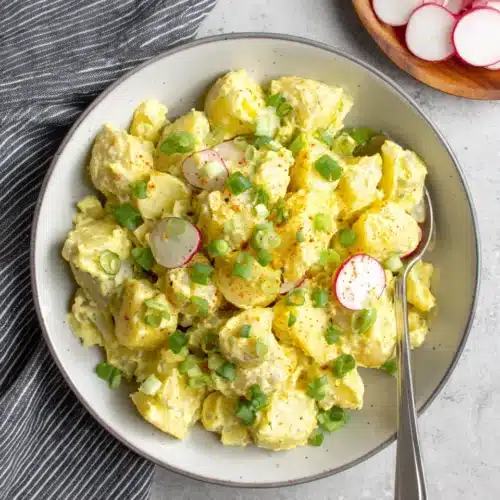 Creamy vegan potato salad in a bowl with green onions and paprika, served with radishes
