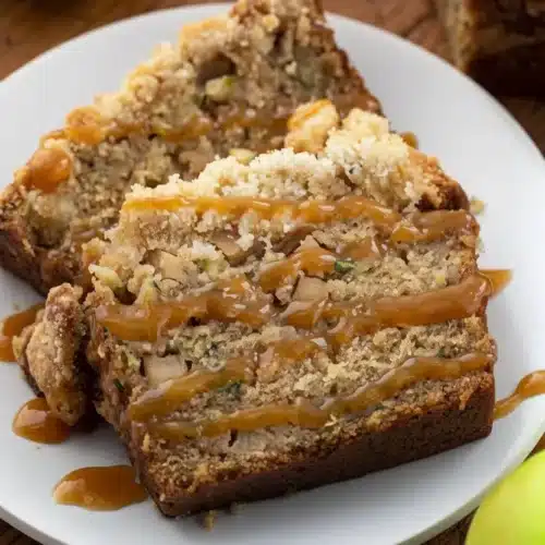 Slices of apple zucchini bread with caramel drizzle and crumb topping on a white plate