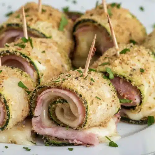Baked zucchini rolls with cheese, ham, and herbs on a white plate