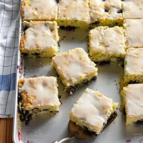 Blueberry zucchini bars with white icing on a baking sheet, some cut and served.
