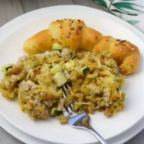 Chicken zucchini stuffing mix casserole served on a white plate with a croissant and fork
