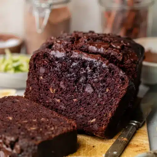 Moist chocolate banana zucchini bread with chocolate chips, sliced on a wooden board with banana and zucchini nearby
