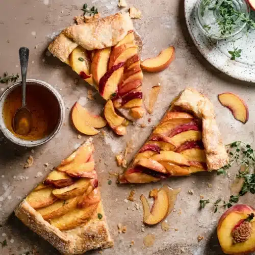 Slices of galette with peach slices on a rustic surface with honey and herbs