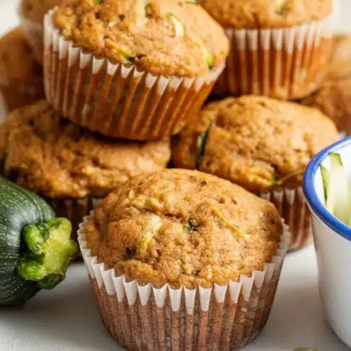 Healthy zucchini muffins in paper liners with fresh zucchini nearby