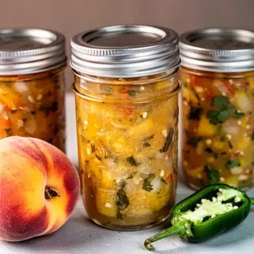 Homemade peach salsa in jars with fresh peaches and jalapeños