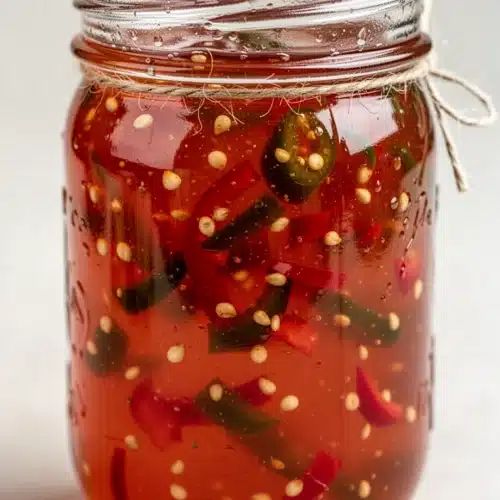 Jalapeño pepper jelly in a glass jar with a spoon, showcasing its spicy, sweet texture