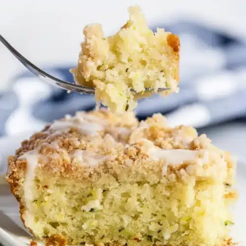 Moist lemon zucchini coffee cake with crumb topping and glaze on a white plate