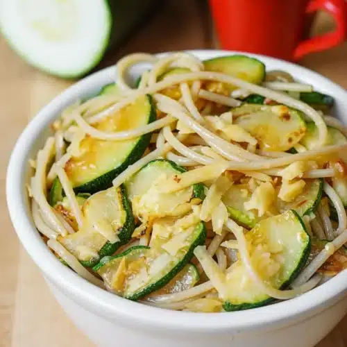 Parmesan zucchini garlic pasta in a white bowl with fresh zucchini and red mug