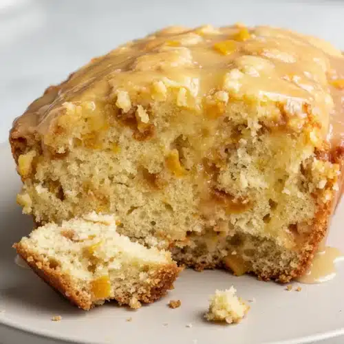 Moist peach cobbler bread with white chocolate glaze, showcasing juicy peaches and fluffy texture