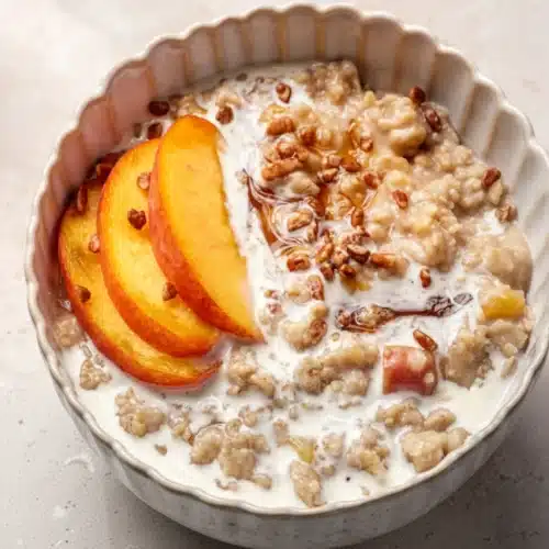 Peaches and cream oatmeal in a bowl with fresh peach slices and nuts