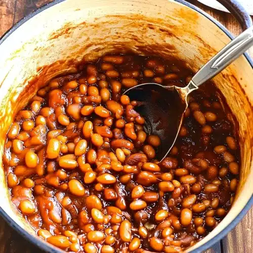 Smoky, sweet homemade beans in a Dutch oven with a serving spoon