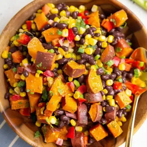 Sweet potato black bean salad with corn, peppers, and cilantro dressing in a wooden bowl