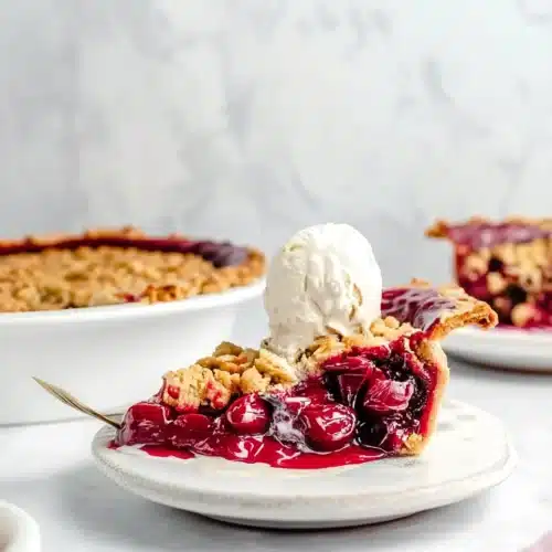 A slice of tart cherry pie topped with vanilla ice cream, served on a white plate.