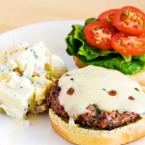 Juicy turkey burger with melted cheese, lettuce, tomato, and potato salad on a plate