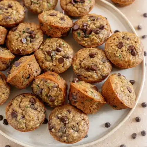 Whole wheat banana zucchini chocolate chip muffins on a plate with chocolate chips scattered around