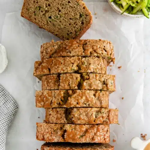 Sliced zucchini bread with applesauce on parchment paper with shredded zucchini nearby