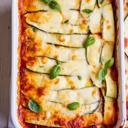 Zucchini lasagna with melted cheese and fresh basil in a white dish