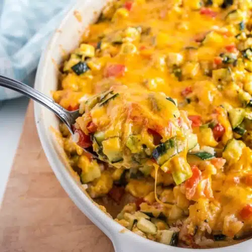 Zucchini tomato casserole with rice in a white dish, topped with melted cheese, being served with a spoon