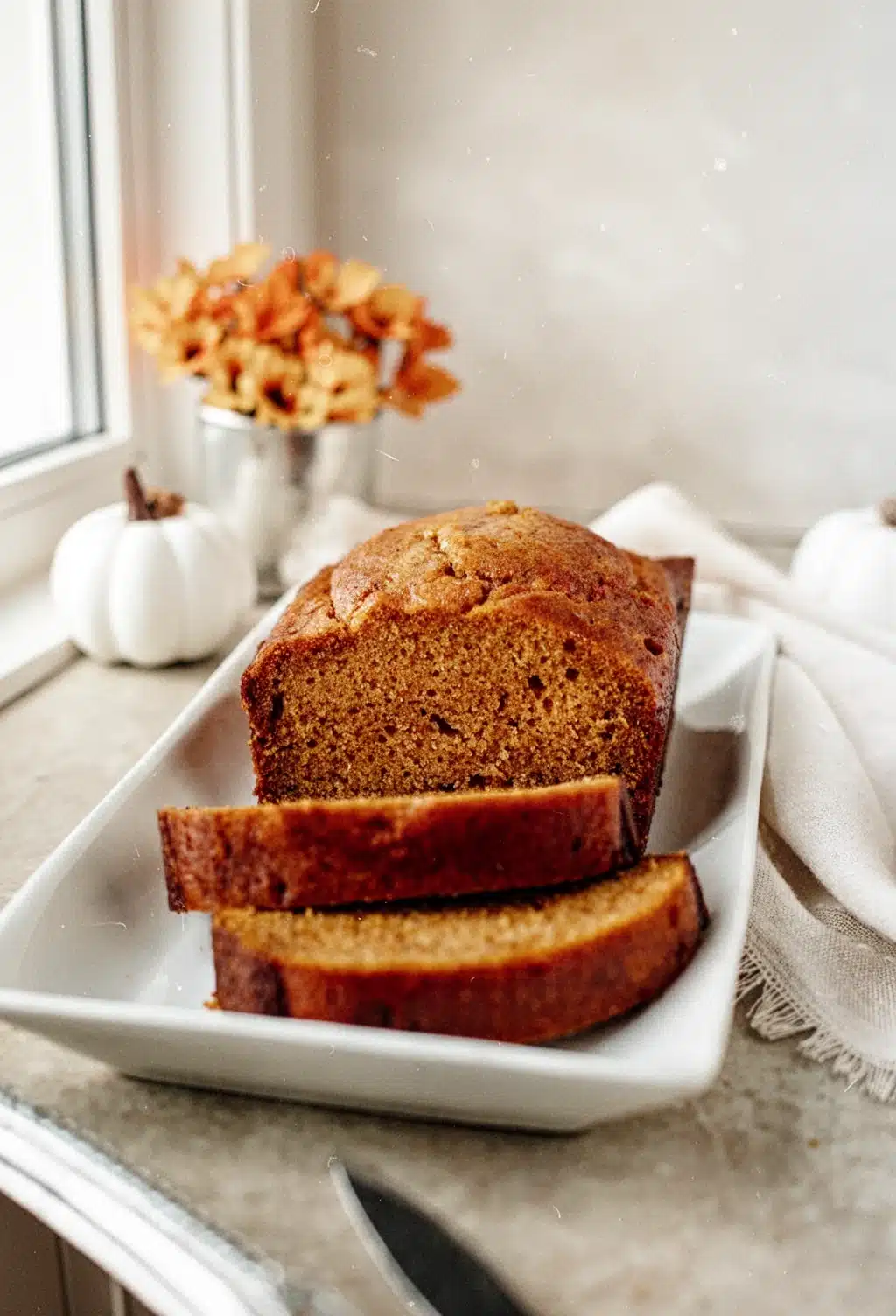 Best Easy Pumpkin Bread Recipe Sliced and Ready to Serve Moist pumpkin bread slices on a white plate with fall decor, best pumpkin bread recipe easy