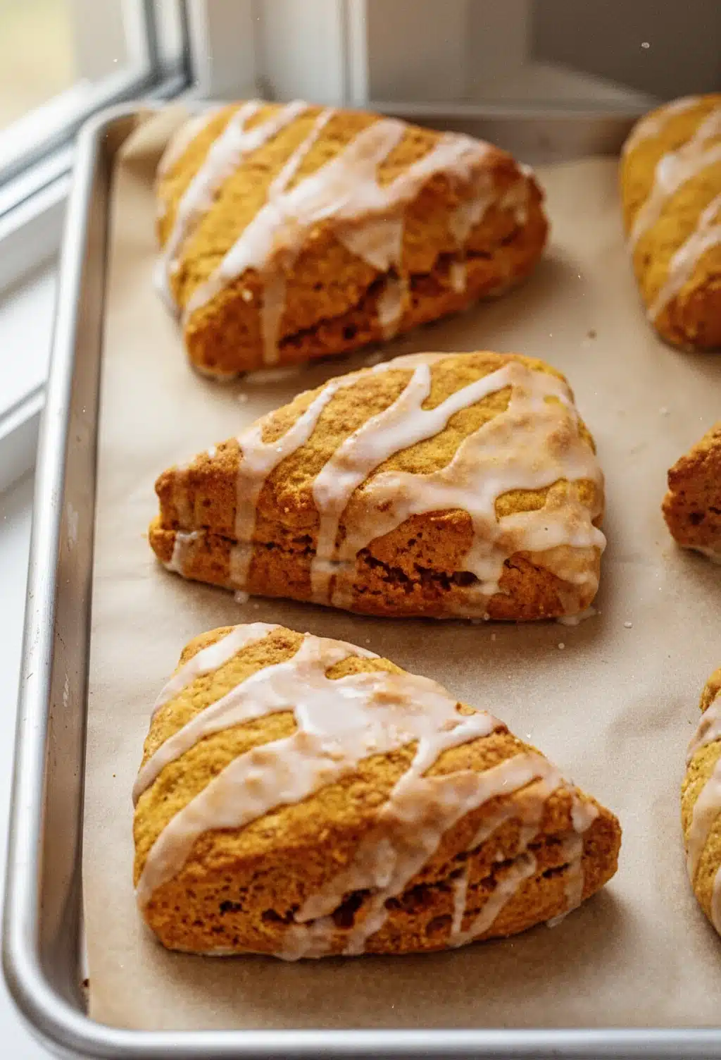 Harvest Pumpkin Scones with Vanilla Glaze Golden harvest pumpkin scones with white glaze on a baking sheet